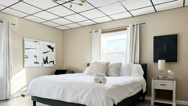 Een moderne slaapkamer met een groot bed, een nachtkastje met een lamp en een raam met gordijnen.