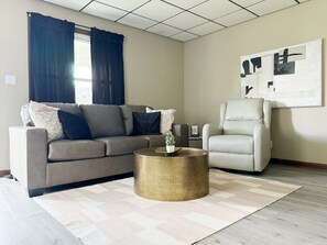 Una sala de estar con un sofá color beige, un sillón blanco, una mesa de centro redonda y un cuadro abstracto grande en la pared.
