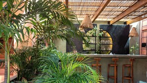 Un espace bar doté d’un comptoir en béton, de tabourets en bois et d’une variété de plantes.