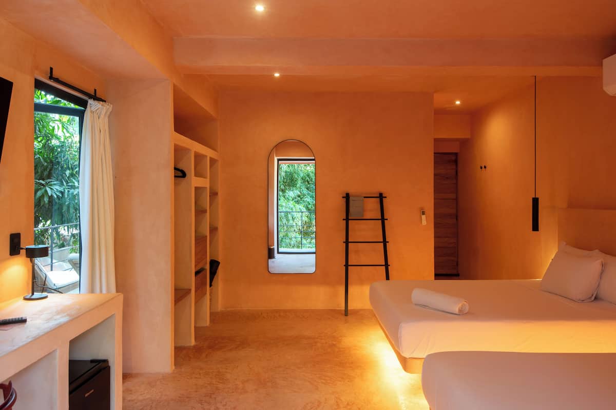 A bedroom with a bed, a desk, a chair, a ladder, and a window with a view of greenery.