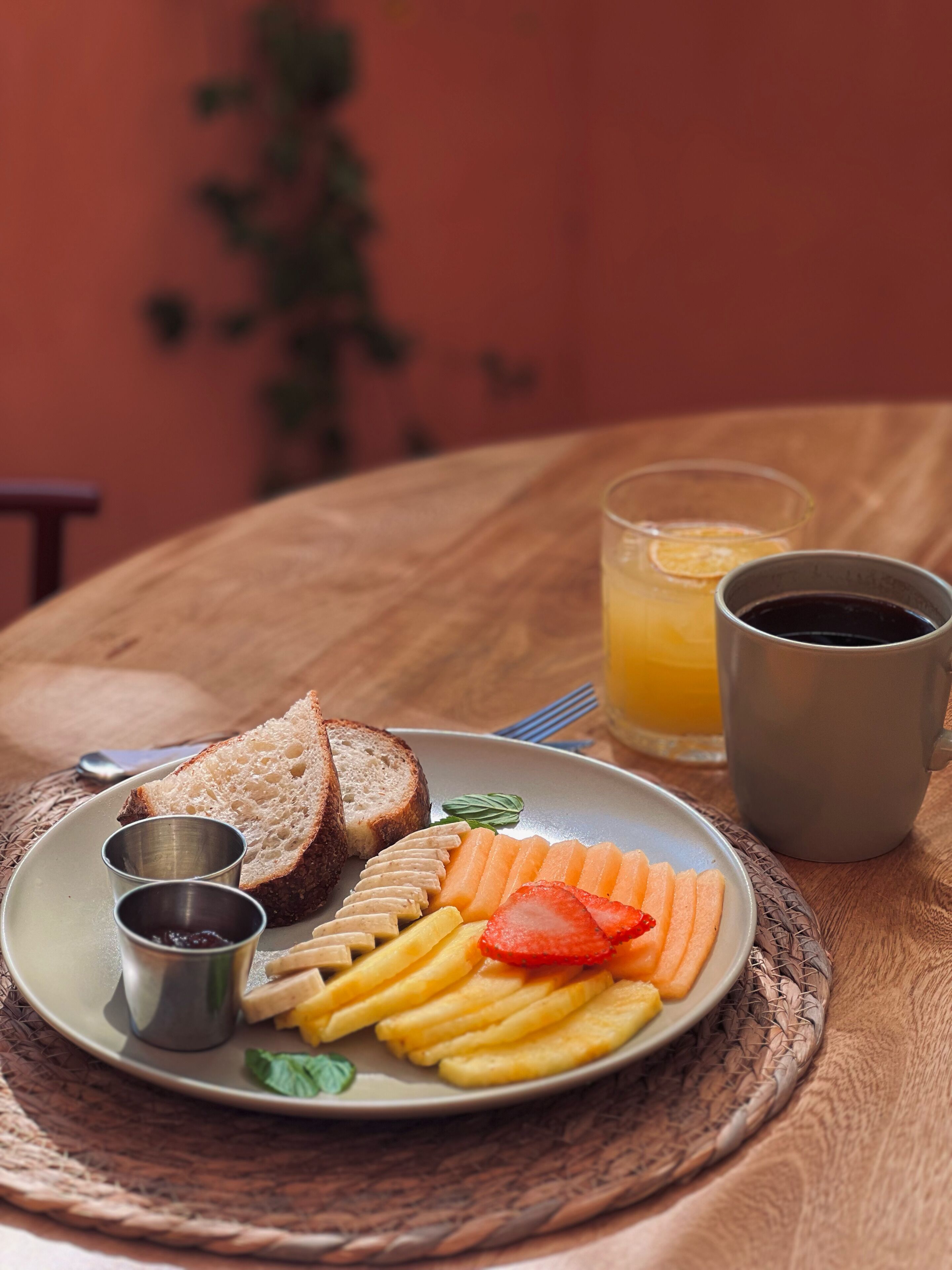 A plate of food with bread, fruit, and fries, a glass of orange juice, and a cup of coffee on a wooden table.
