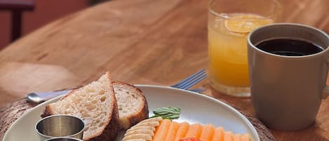 A plate of food with bread, fruit, and fries, a glass of orange juice, and a cup of coffee on a wooden table.