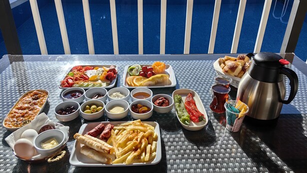 A table with various food items and condiments, including a hot beverage, on a balcony with a view of a pool. - MERAL RESORT 1 (Sapanca)