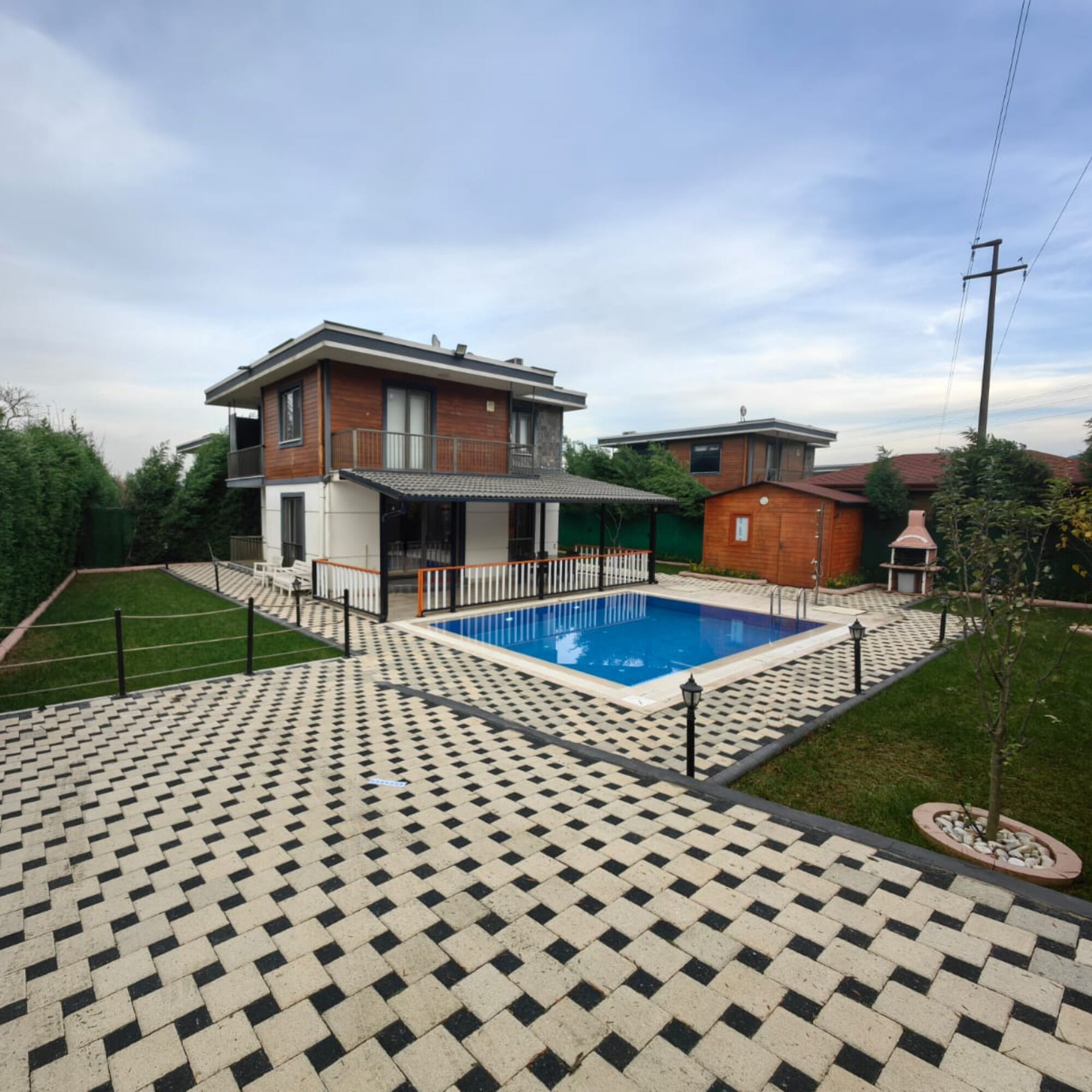 A modern two-story house with a swimming pool, surrounded by a patterned patio and a small garden.