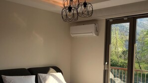 A bedroom with a large bed, white linens, a modern chandelier, an air conditioning unit, and a balcony with a view of trees. - MERAL RESORT 1 (Sapanca)