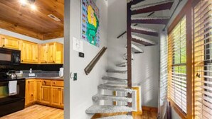 Una cocina con armarios de madera y un microondas, una escalera con un rascador para gatos, y una ventana con persianas.