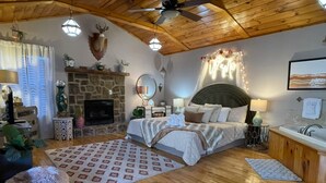 Un dormitorio acogedor con chimenea de piedra, una cama con cabecera, una mesita de noche y una ventana con cortinas.