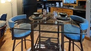 Una cocina moderna con armarios de madera, un refrigerador negro y un comedor con mesa de vidrio y sillas azules.