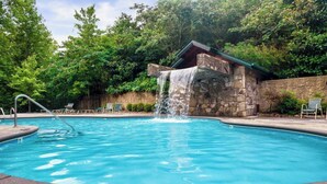 A swimming pool with a waterfall feature, surrounded by stone walls and greenery.