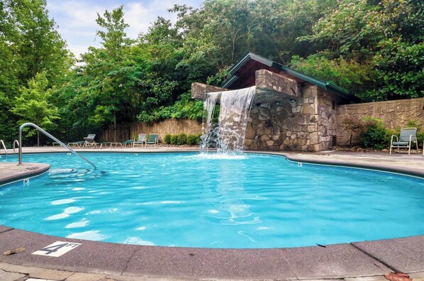 A swimming pool with a waterfall feature, surrounded by stone walls and greenery.
