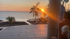 A sunset view from a terrace with tiled flooring, palm trees, and a pool area.