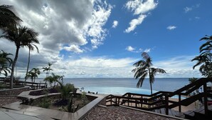 A stone pathway leading to a pool with a view of the ocean and palm trees.