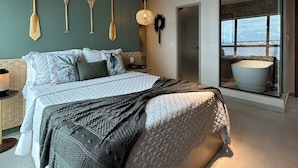 A modern bedroom with a large bed, a view of the sea through a glass door, and a unique wall decoration of wooden paddles.