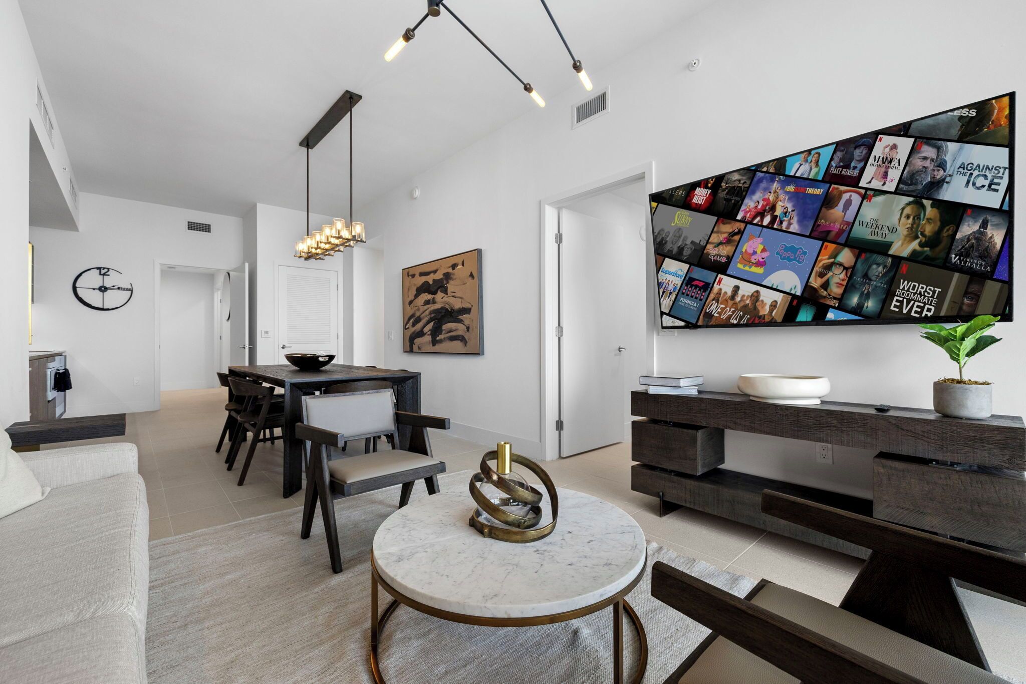 A modern living room with a large TV displaying movie posters, a dining area with a white table and dark chairs, and a minimalist decor style.