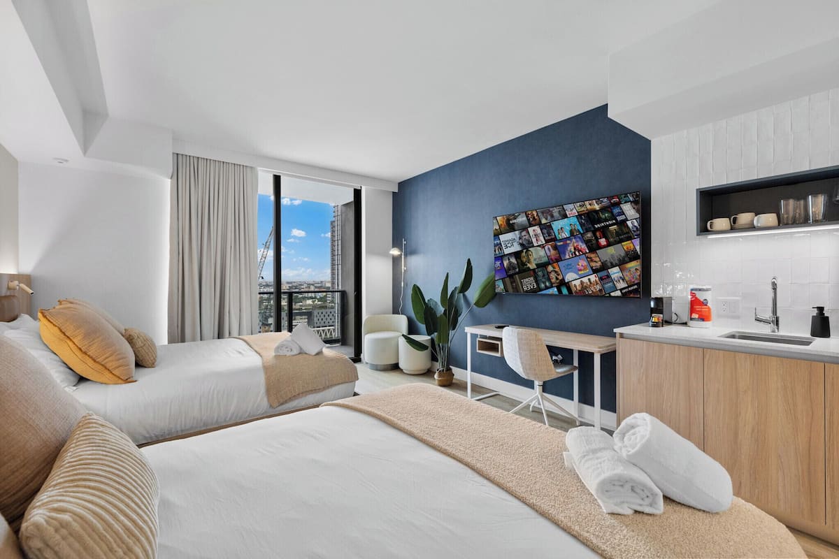 A modern hotel room with a large bed, a desk, a view of the city, and a wall art display.