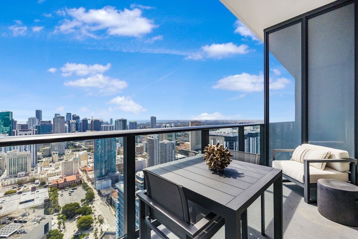 A balcony with a table and chairs, overlooking a cityscape with tall buildings.