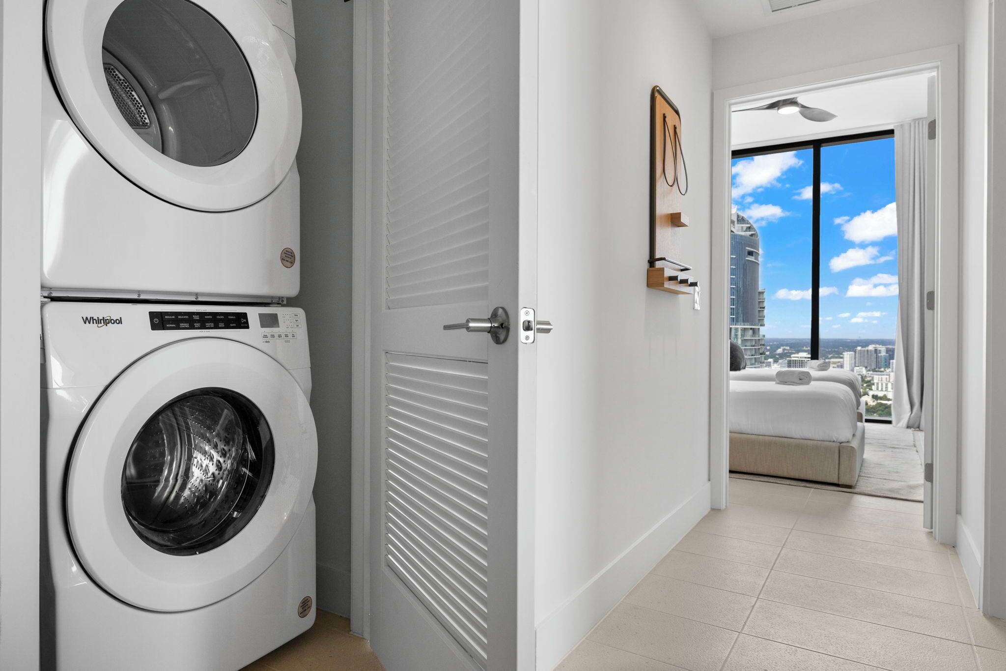 A laundry room with a Whirlpool washer and dryer, a door leading to a balcony with a city view.