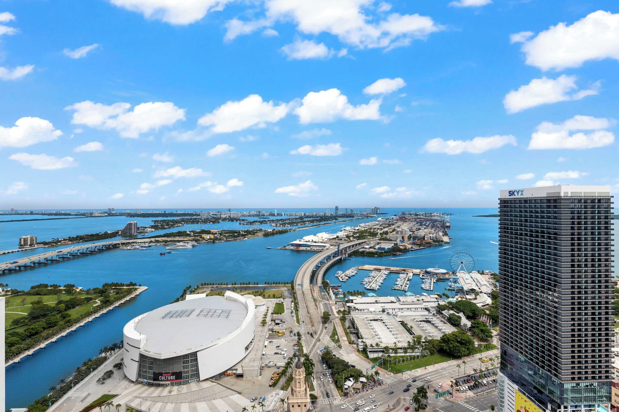 Une vue urbaine sur le front de mer, avec un bâtiment moderne, un grand stade et un port de plaisance.