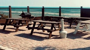 A beachside patio with picnic tables and a barbecue grill, overlooking the ocean. - Cozy new Daytona Beach studio with pool access,sunset and ocean views. (Daytona Beach)