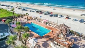 A beach resort with a swimming pool, beach chairs, umbrellas, and a view of the ocean. - Cozy new Daytona Beach studio with pool access,sunset and ocean views. (Daytona Beach)