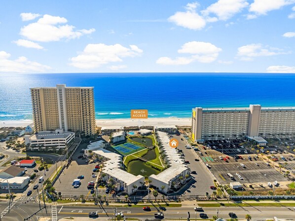 A beachfront hotel with multiple high-rise buildings, a parking lot, and a pool area.