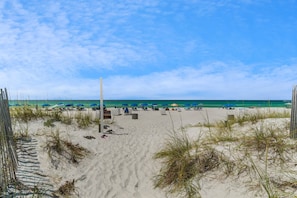 A beach with umbrellas and lounge chairs, a sandy path, and a view of the ocean.