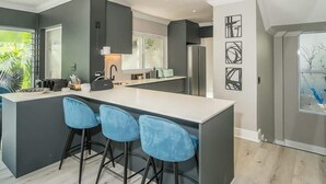 A modern kitchen with a central island, bar stools, and a large window.