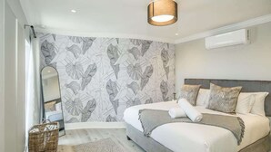 A bedroom with a bed, a mirror, a wall-mounted air conditioner, and a ceiling light fixture.