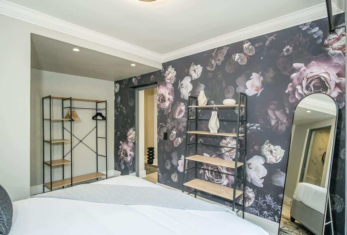 A bedroom with a bed, a wardrobe, a mirror, and a floral wallpaper.