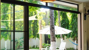 Comedor con una laptop sobre la mesa, un posavasos tejido y vistas a una piscina y follaje exterior.