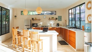 Una cocina moderna con una isla central, sillas de madera, una laptop y un amplio ventanal.