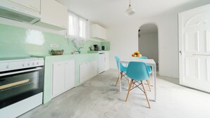 Cozinha moderna com armários brancos, painel de parede verde e área de refeições com cadeiras azuis.