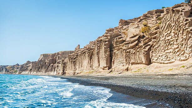 Paisagem costeira com um penhasco rochoso e uma praia.
