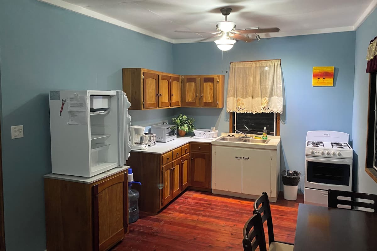 Une cuisine de taille réduite, dotée de meubles en bois, d’un réfrigérateur, d’une cuisinière et d’un ventilateur de plafond.