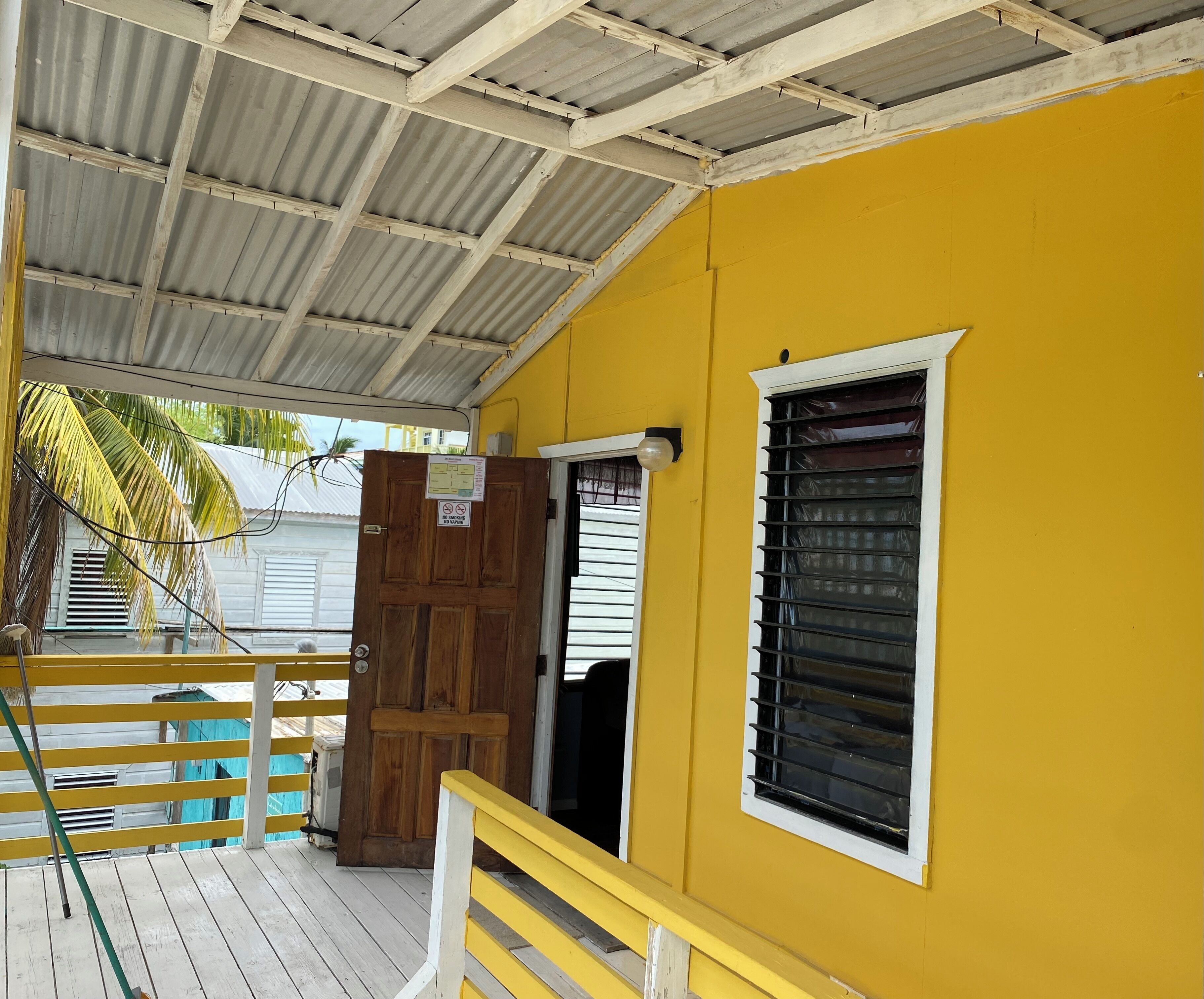 A yellow building with a wooden door, a window with horizontal bars, and a metal roof.