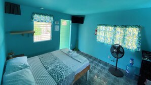 Una habitación con cama, ventana con cortinas, ventilador y dispensador de agua.
