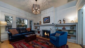 Ein Wohnzimmer mit Kamin, einem blauen Sofa, einem schwarzen Ledersessel und einem gemusterten Teppich.