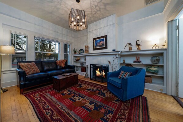 Un salon avec une cheminée, un canapé bleu, un divan en cuir noir et un tapis à motifs.