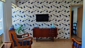 Quarto com um armário de madeira, televisão fixada na parede e papel de parede estampado.