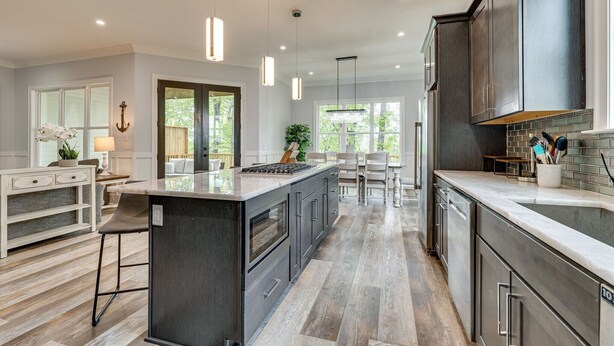 Een moderne keuken met een centraal eiland, hanglampen en een doorkijk naar een eetgedeelte.