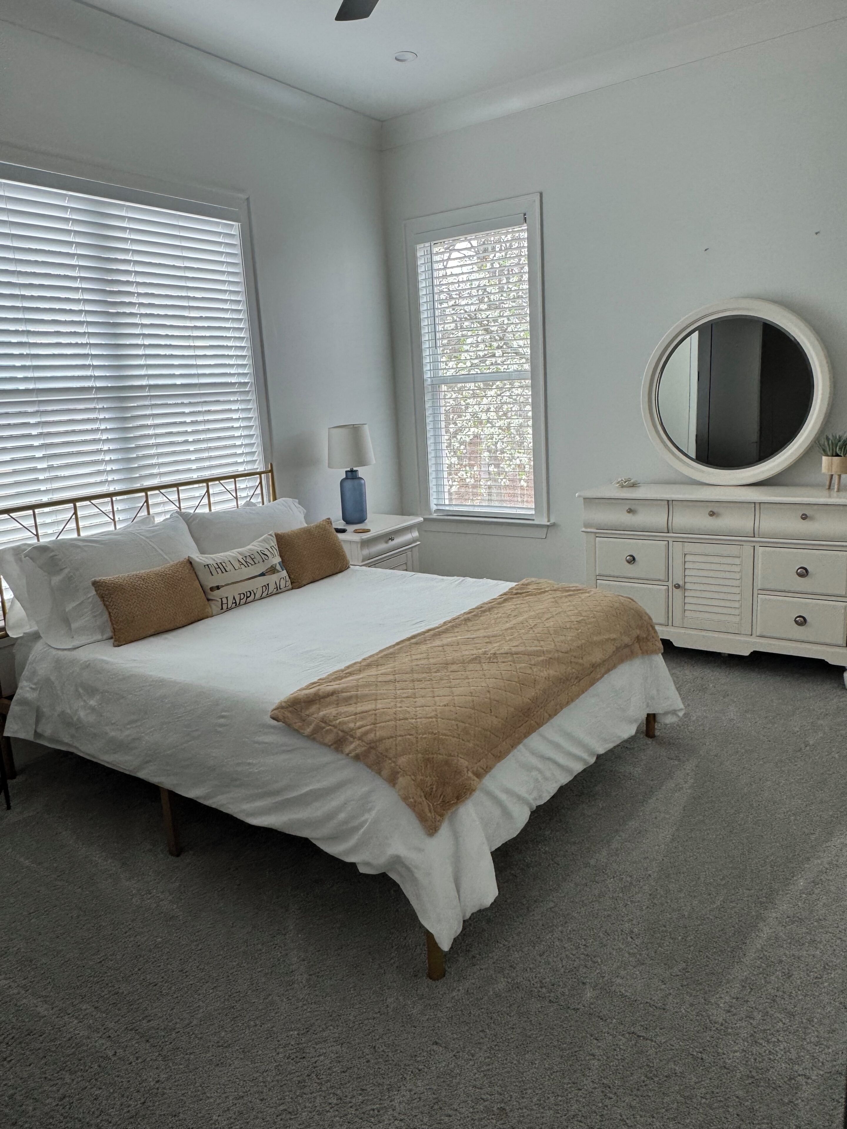 Un dormitorio con cama, mesitas de noche, cómoda y un ventanal grande.