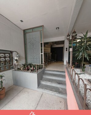 A hotel entrance with a staircase, a decorative wall, and a row of potted plants.