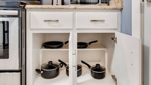 A kitchen with white cabinetry, a microwave, and two black frying pans on open shelves.