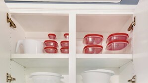 A kitchen cabinet with white shelves, red-lidded containers, and a white colander.