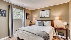 A bedroom with a bed, bedside tables, a window with curtains, a wall art piece, and a ceiling light.