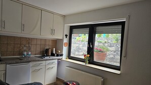 A compact kitchen with white cabinets, a countertop, and a window with blinds.