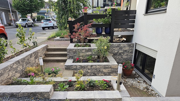 A residential garden with stone planters and steps leading to a house.