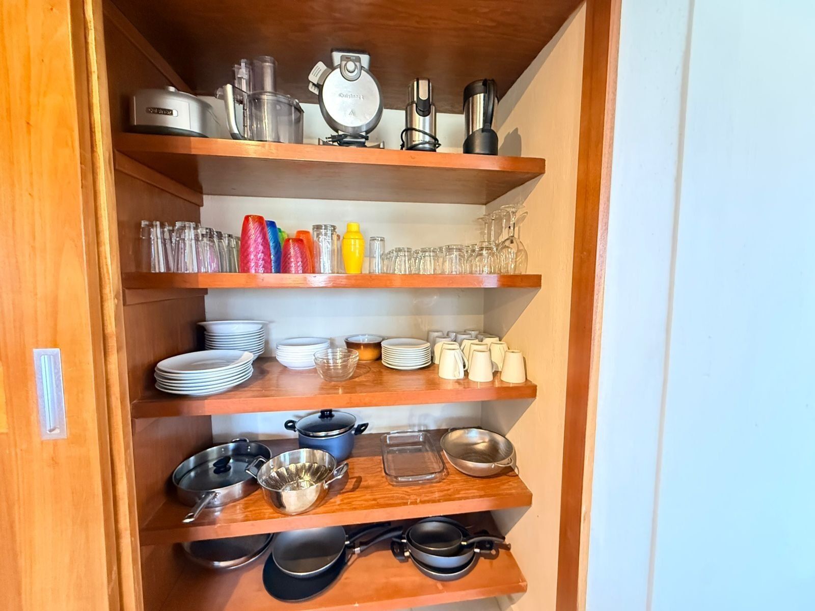 A kitchen with wooden shelves holding various kitchenware, including pots, pans, and glassware.