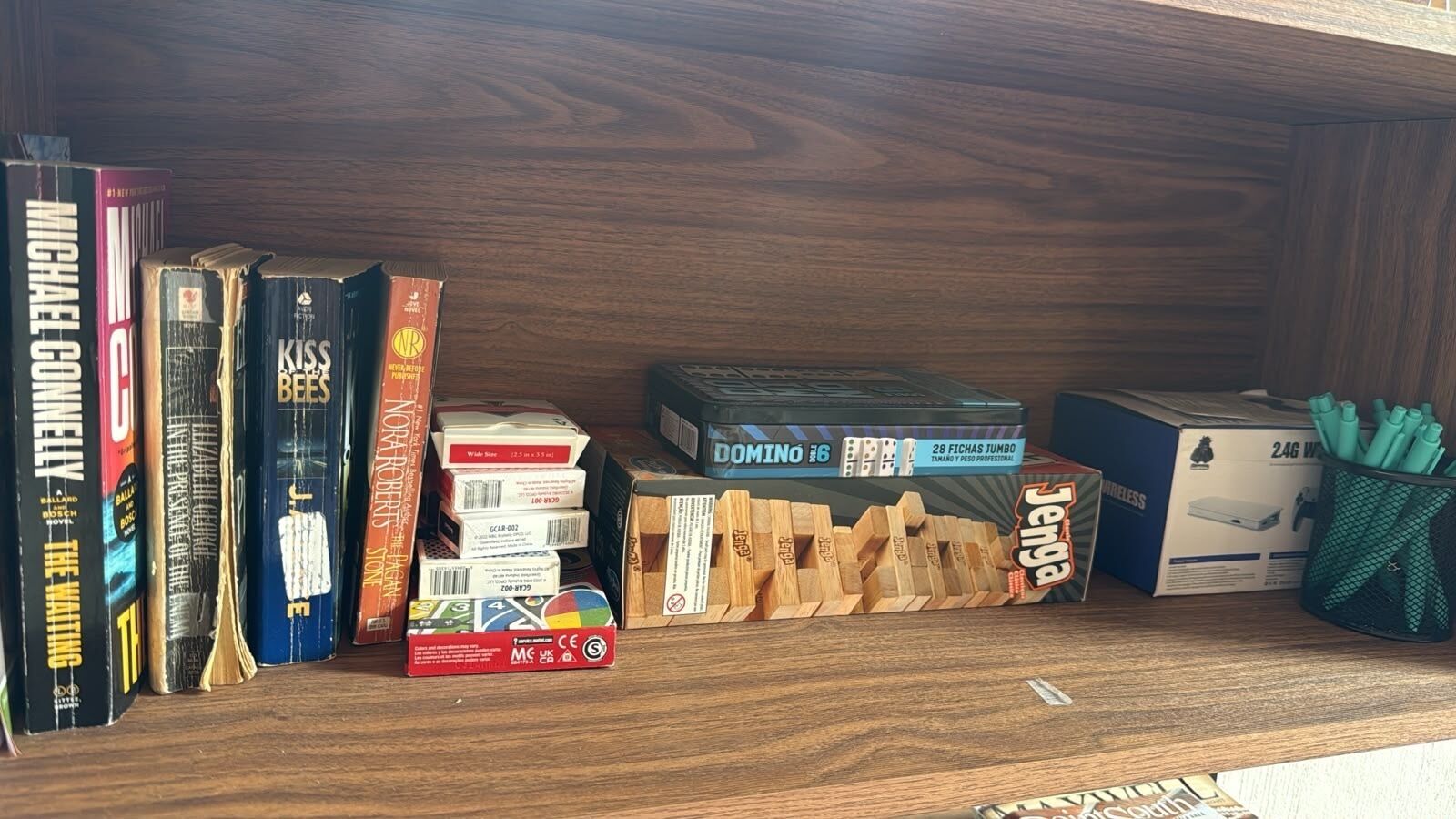 Una estantería con libros, dados de dominó y una base de carga inalámbrica.