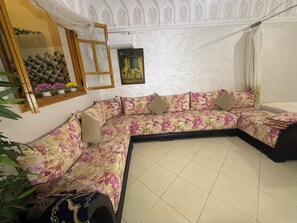 Una habitación con un sofá floral, un espejo, un cuadro enmarcado y una ventana con cortinas.